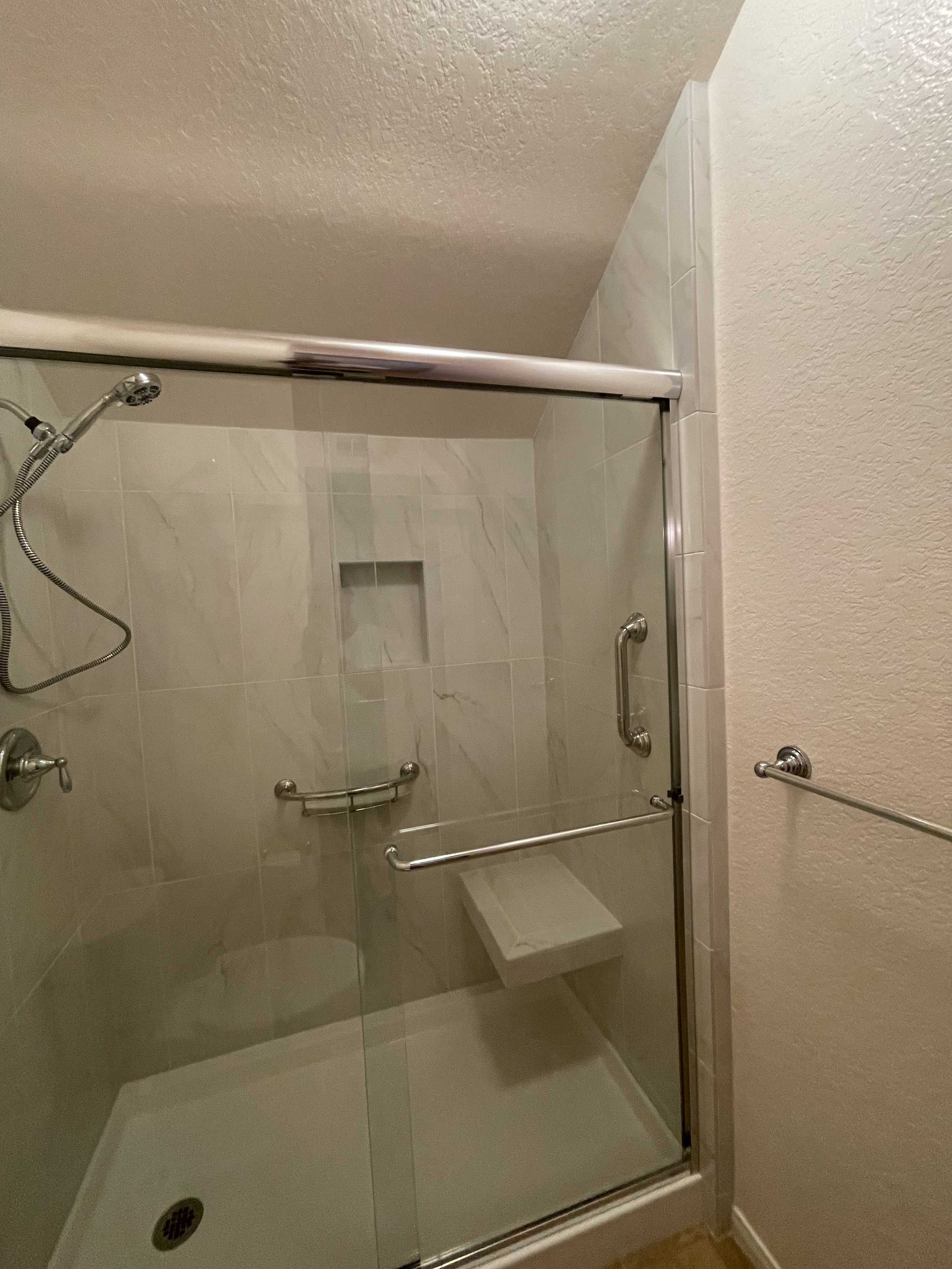 A shower stall with glass door, tiled walls, a handheld showerhead, and a built-in niche for toiletries.