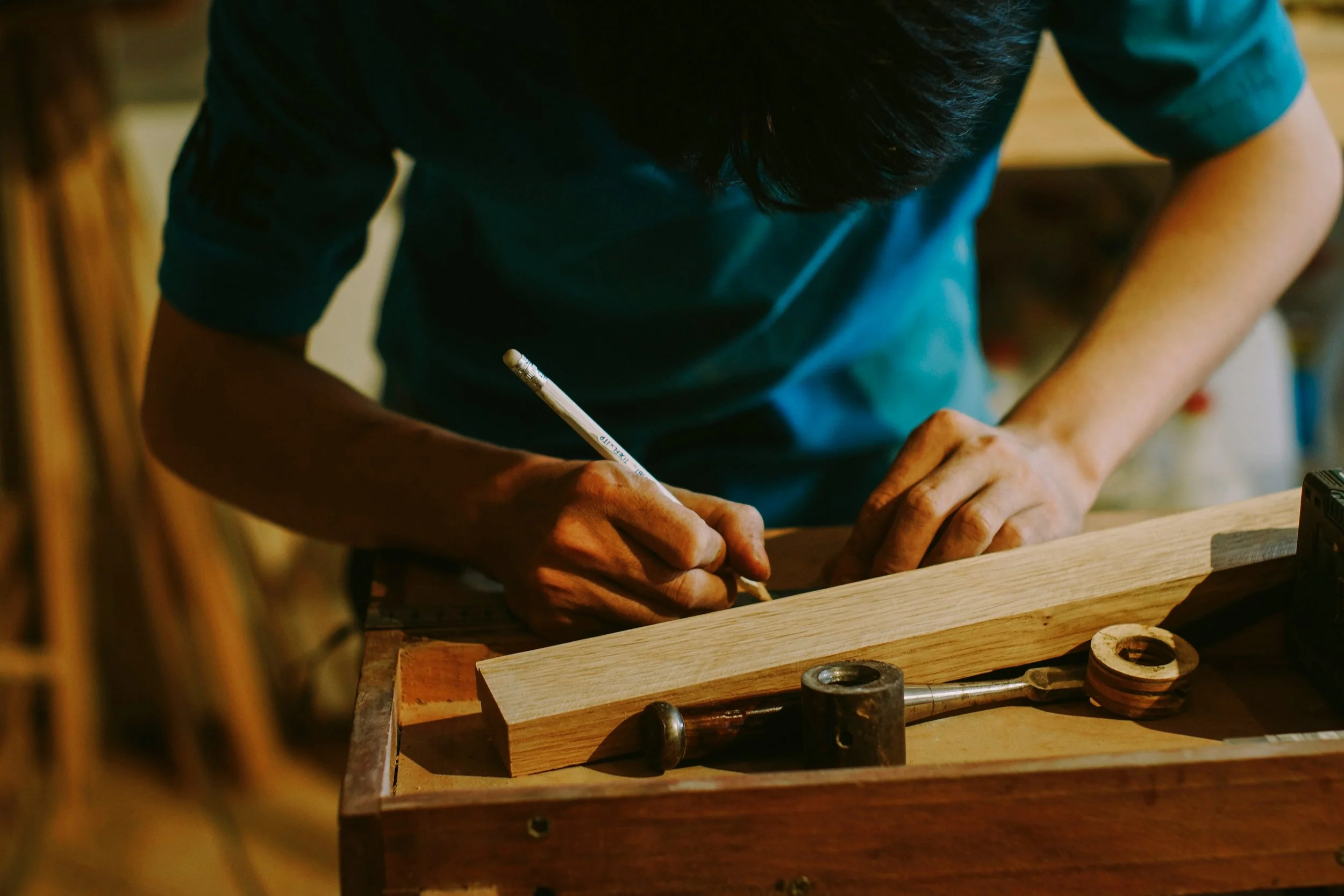 Person working on a woodworking project, measuring or marking a piece of wood in a workshop.