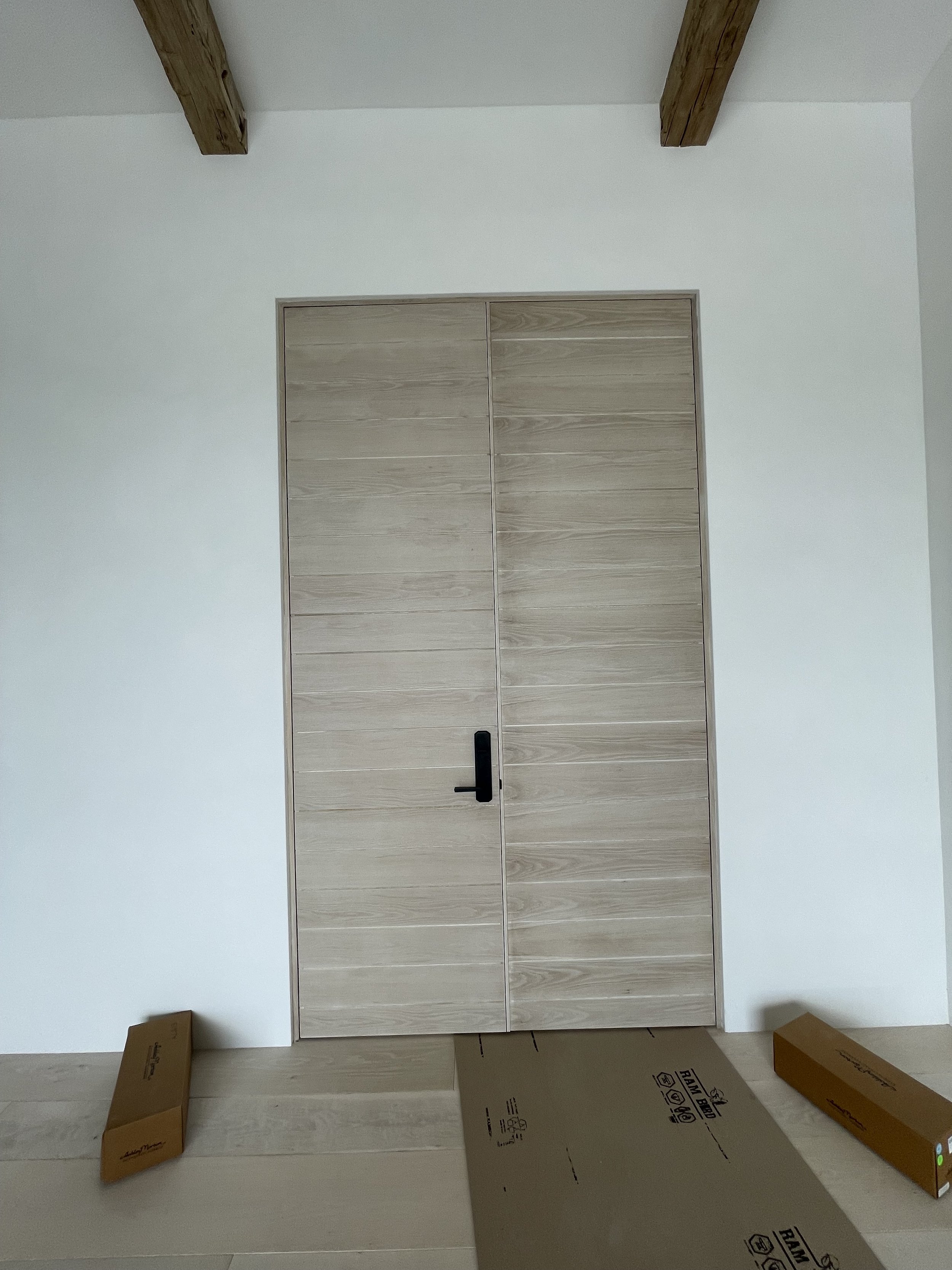 A wooden door with a black handle set within a white wall. Two cardboard boxes are on the floor, one on each side of the door.