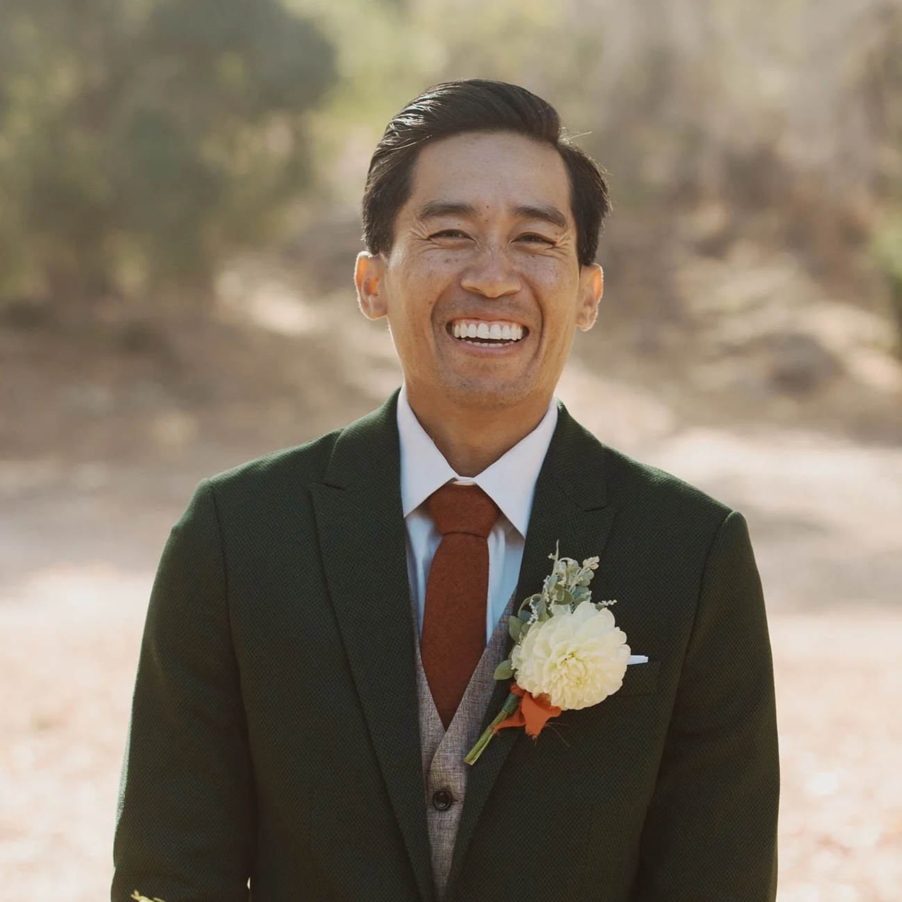 A man in a suit with a boutonniere smiling outdoors.