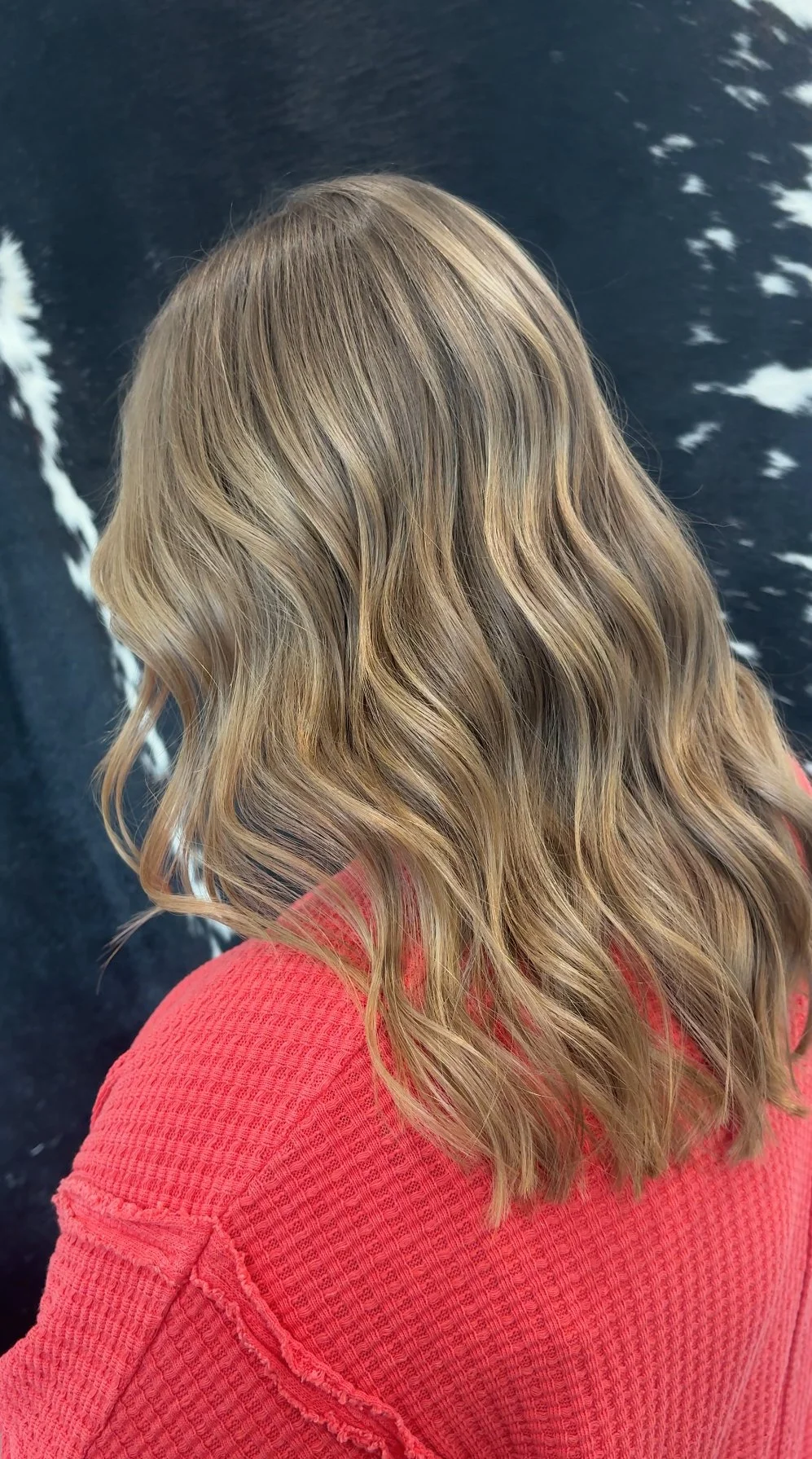 The image shows a woman with long, wavy blonde hair wearing a red textured top, standing against a dark background with white markings.