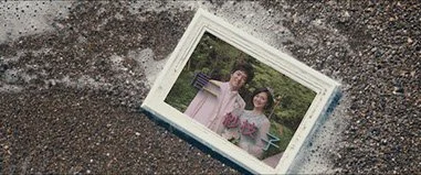 泥の地面の上に置かれた写真アルバムのページに、2人の女性が写っている写真がはめ込まれている