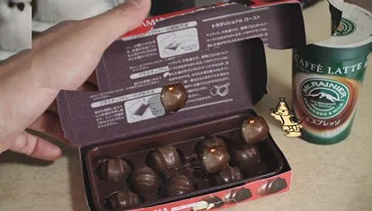 手に持ったチョコレートの箱とコーヒーカップ