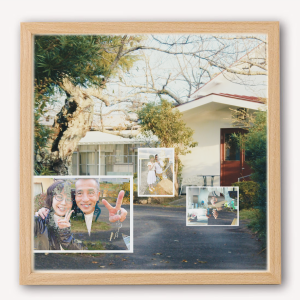 木と家の前に置かれたガラス写真枠に家族写真が複数飾られている風景