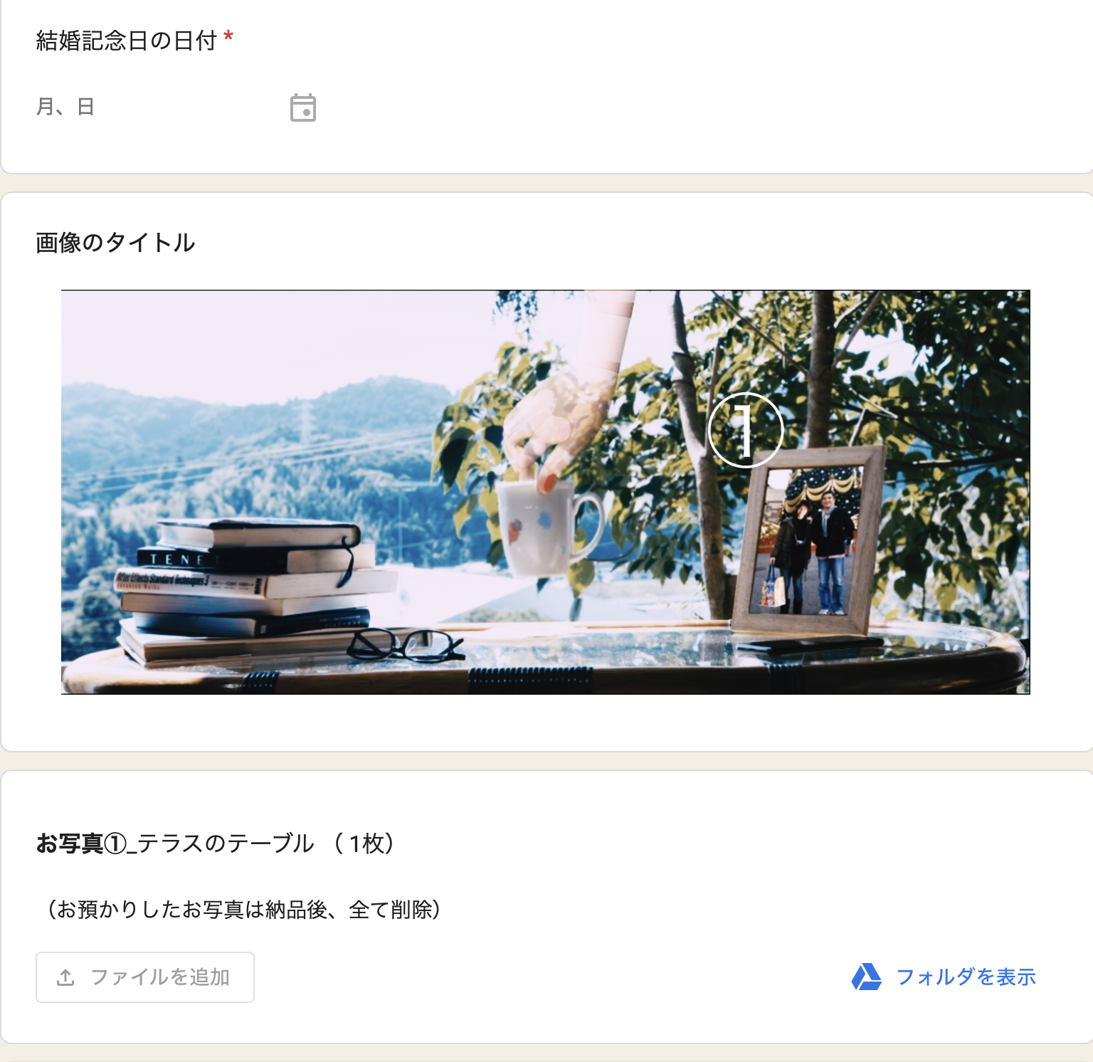 テラスの上に置かれた本や眼鏡と、手がコーヒーカップを持ち上げている様子の写真。背景には山と空と木々、テーブルには写真立てが置かれている。