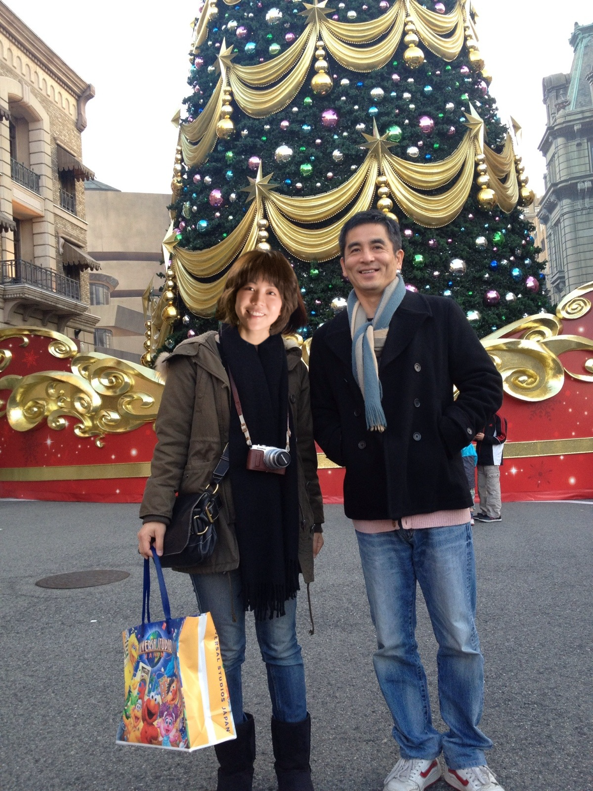 大型のクリスマスツリーの前で笑顔の男女二人が写っている。