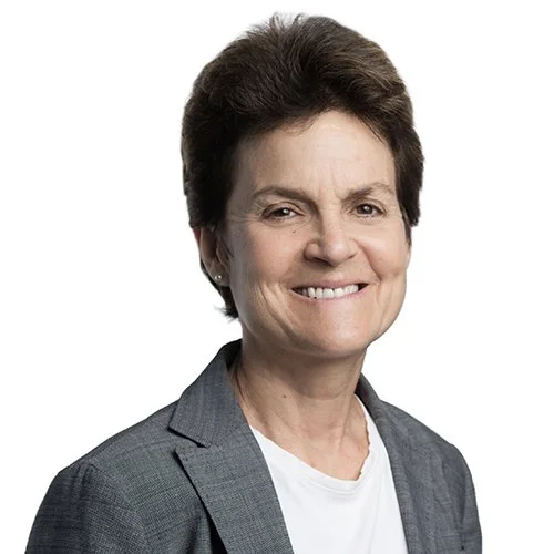 Abby Arnold has light skin, dark short hair, and brown eyes. She is smiling and wearing a grey blazer and white shirt.