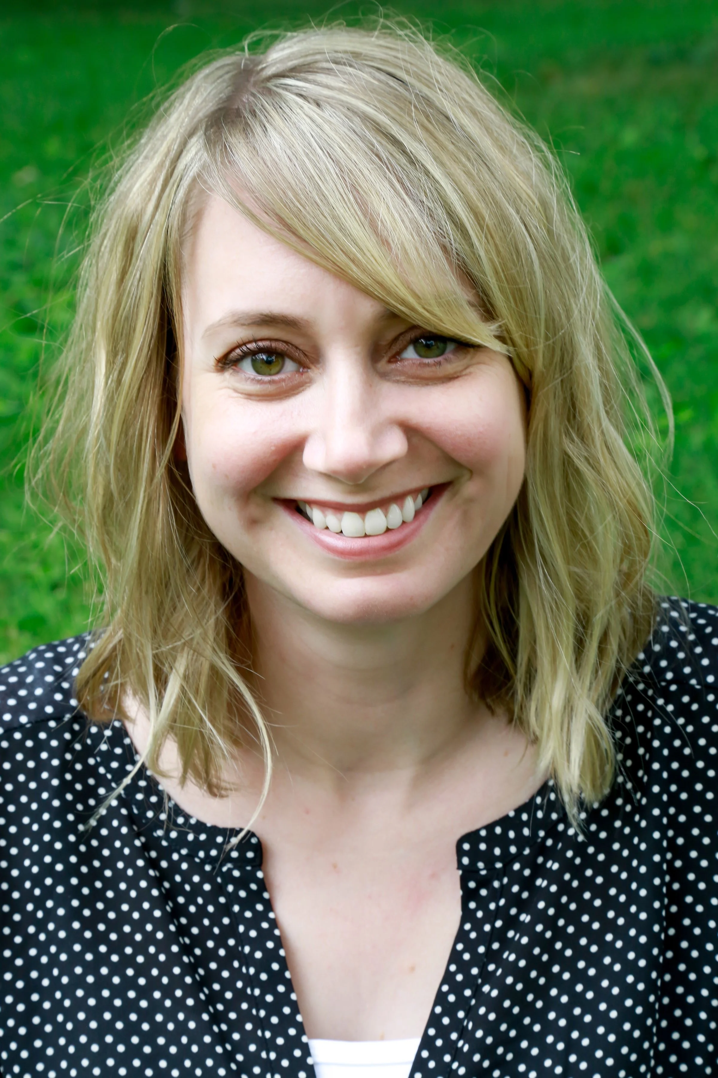 Emily Haley, Founder. Emily has blonde hair, hazel eyes and light skin. She is smiling, wearing a polka dot blouse and is outside.
