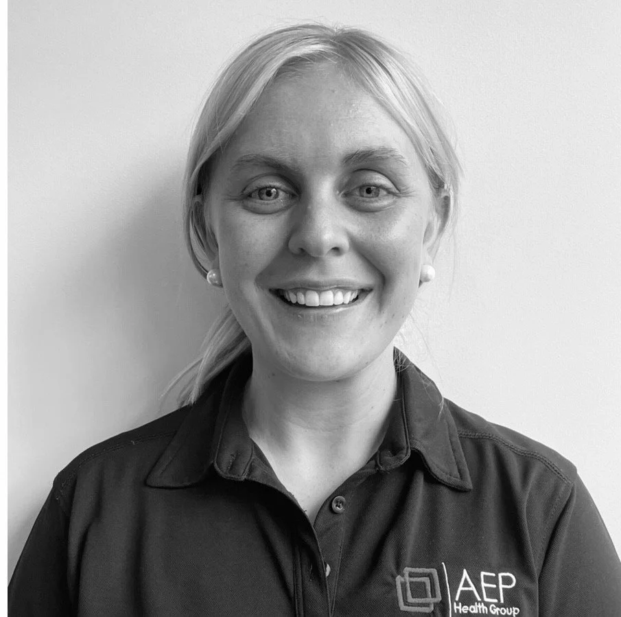 Black and white portrait of a smiling woman with shoulder-length blonde hair, wearing a collared shirt with an "AEP Health Group" logo.