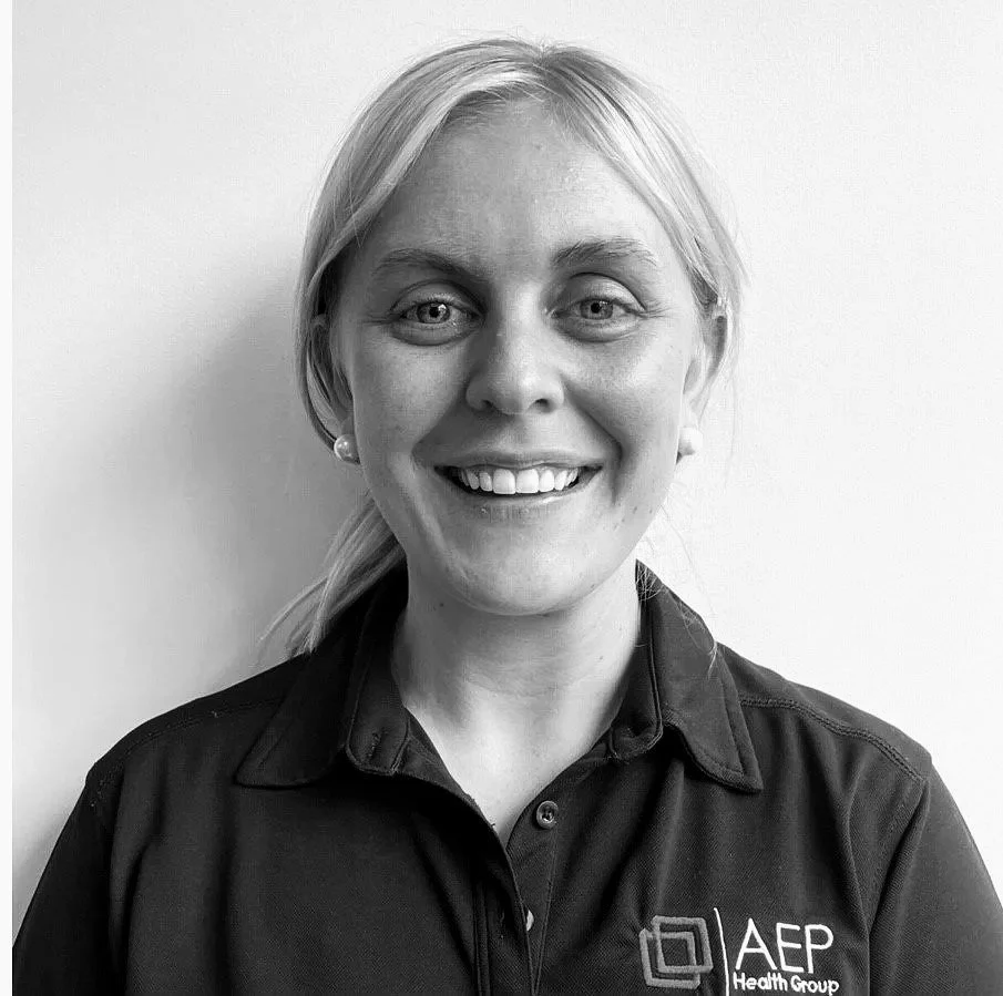 Black and white portrait of a smiling woman with shoulder-length blonde hair, wearing a collared shirt with an "AEP Health Group" logo.