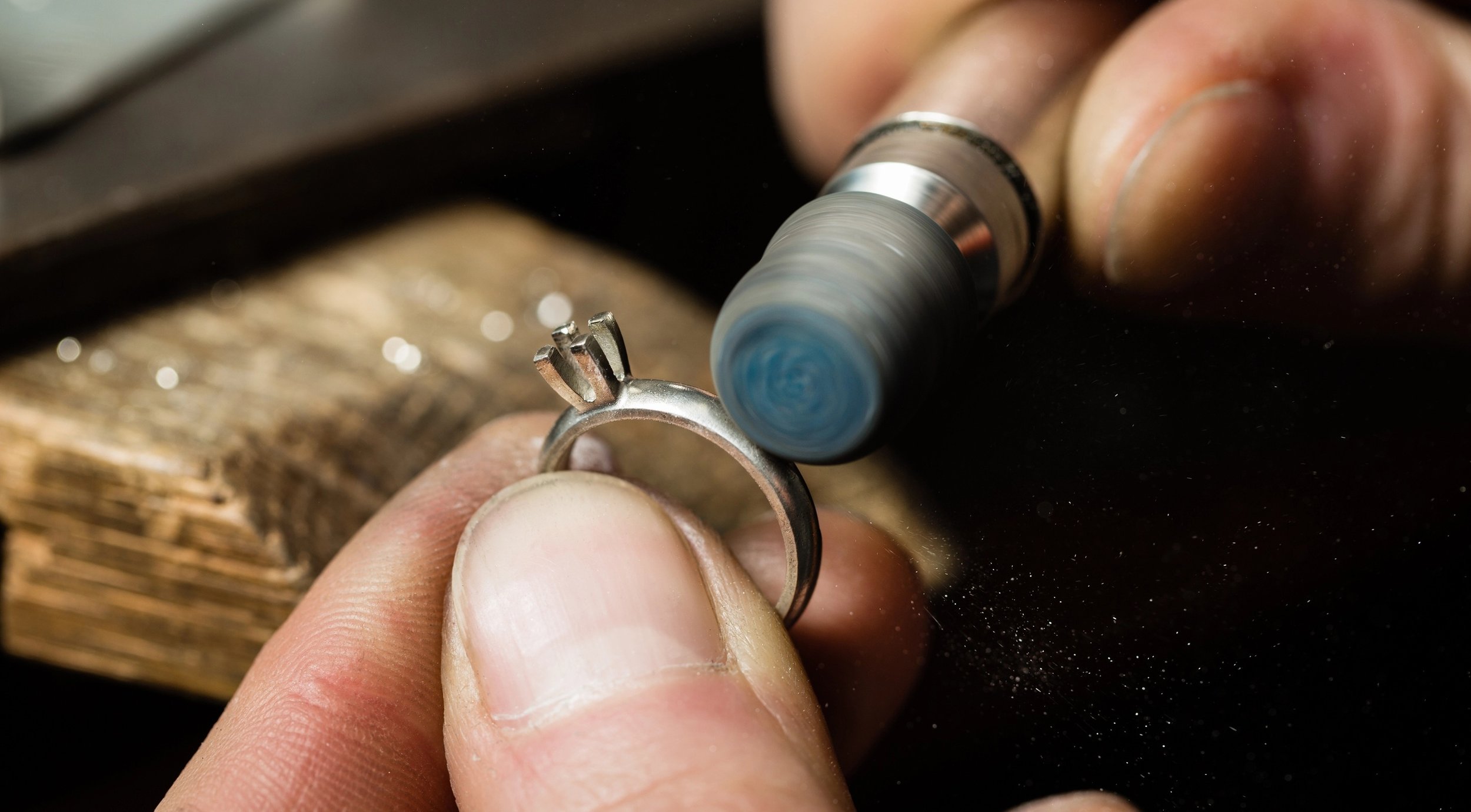 Close-up of a person's hand holding a ring while a rotary tool engraves it.