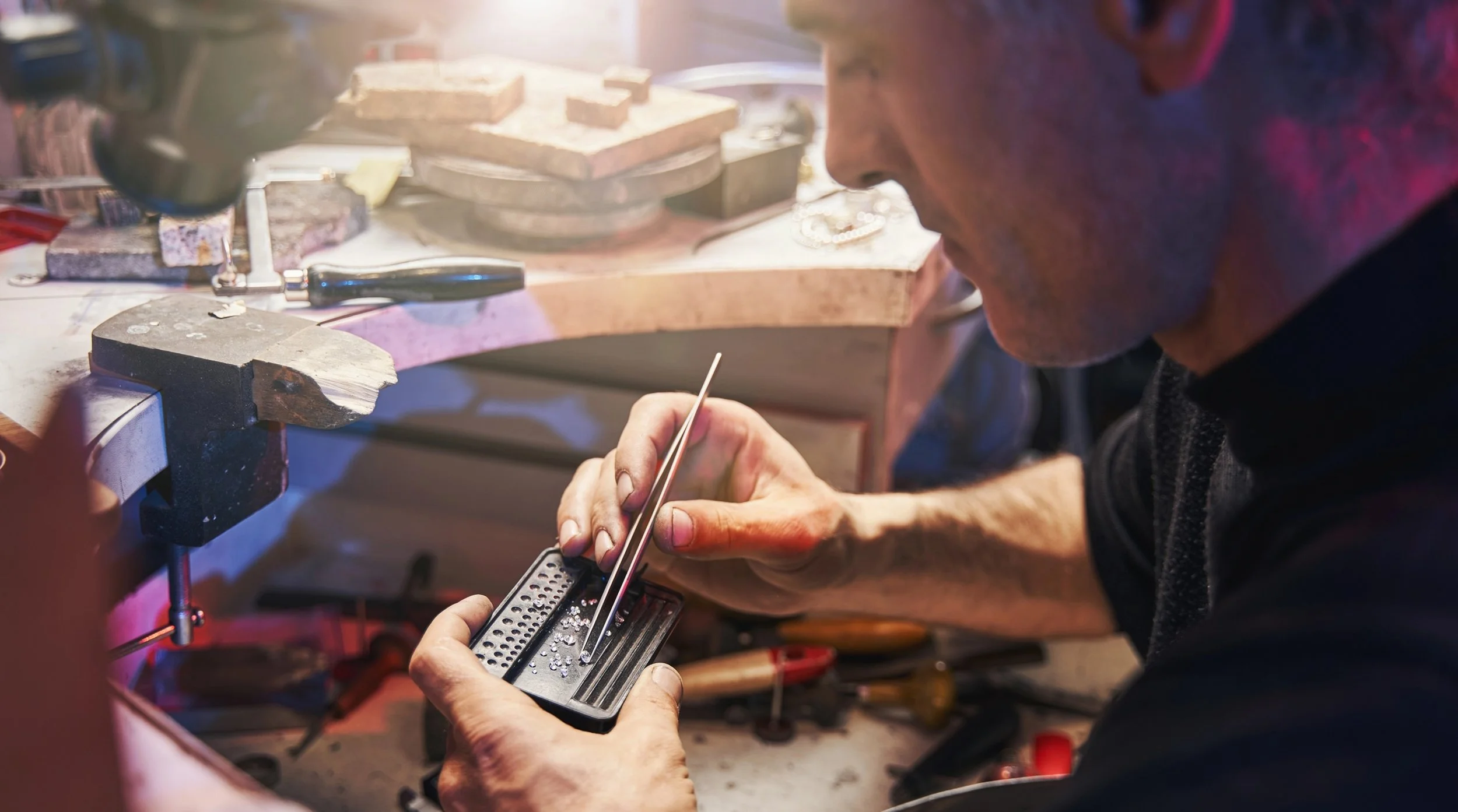 A person working at a jewelry workshop, using a magnifying tool to examine a piece of jewelry.