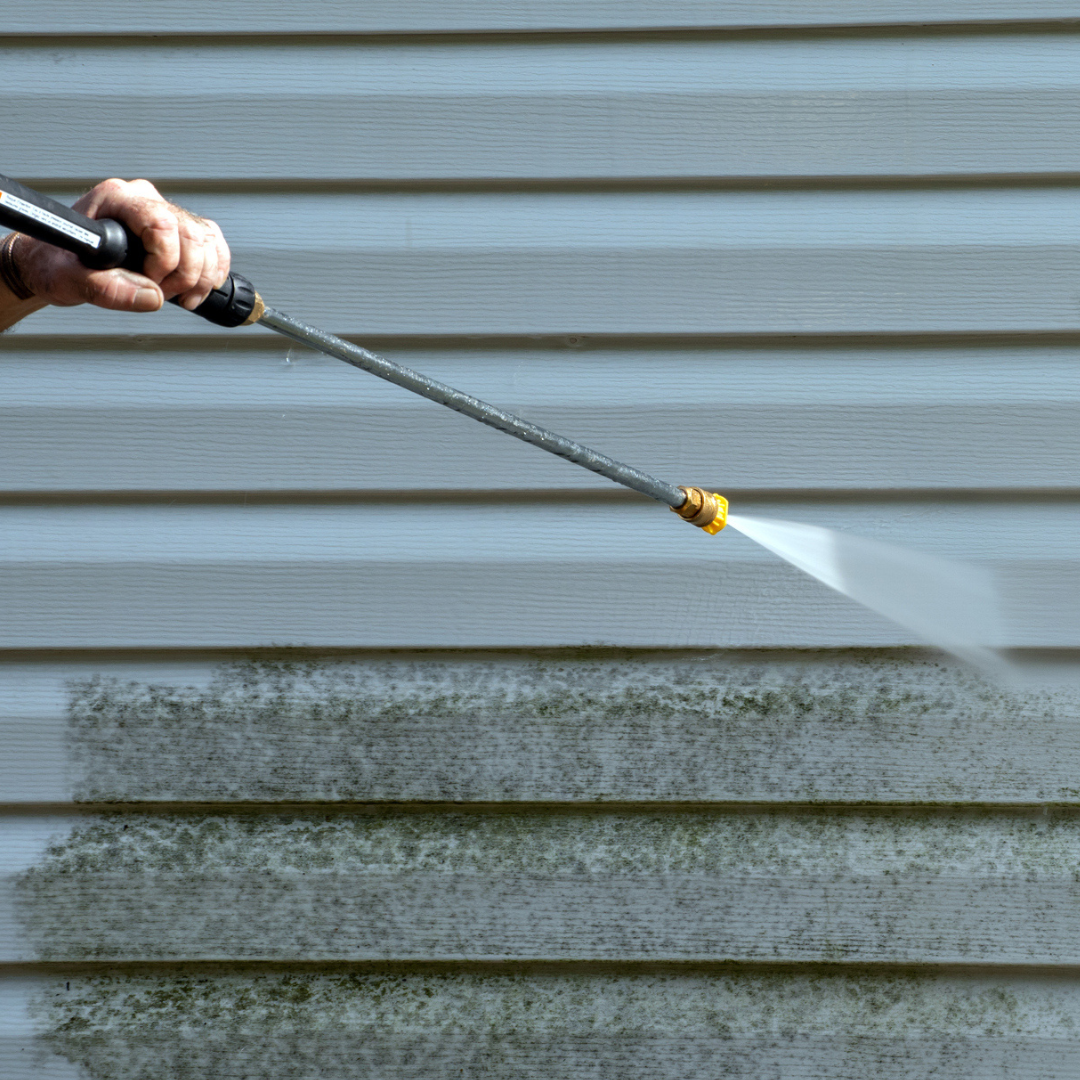 Person using a pressure washer to clean mold and dirt from the siding of a house.