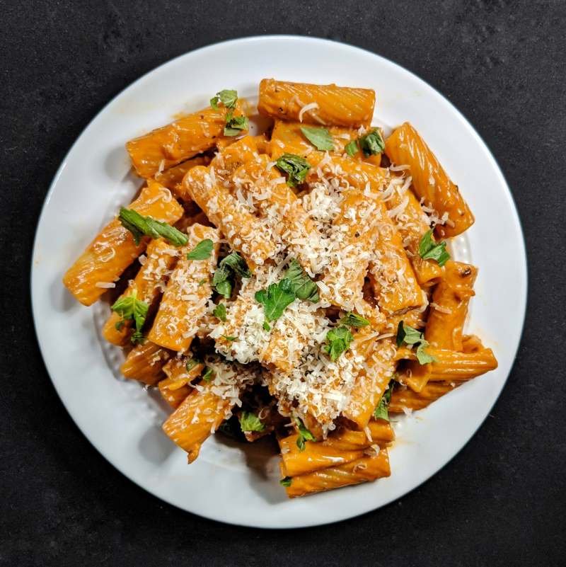 Plate of rigatoni pasta with tomato sauce, grated cheese, and garnished with fresh herbs.
