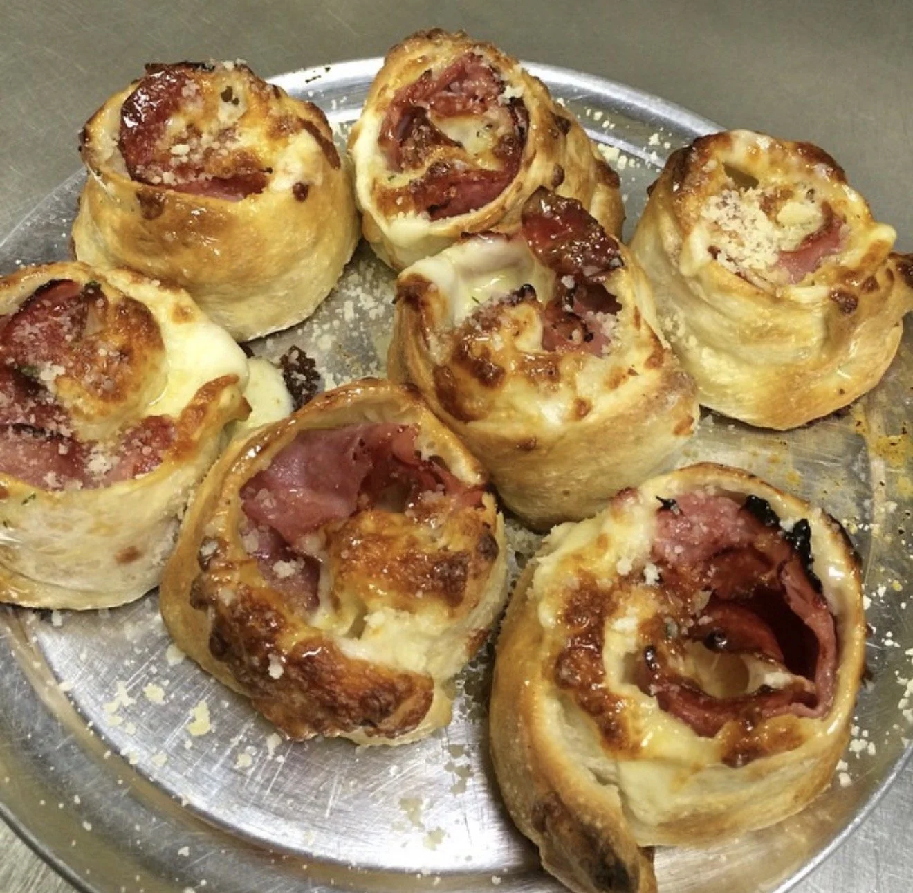 Mini pepperoni and cheese pizzas made with pizza dough rolled into small cups, topped with pepperoni slices and melted cheese, served on a silver tray.