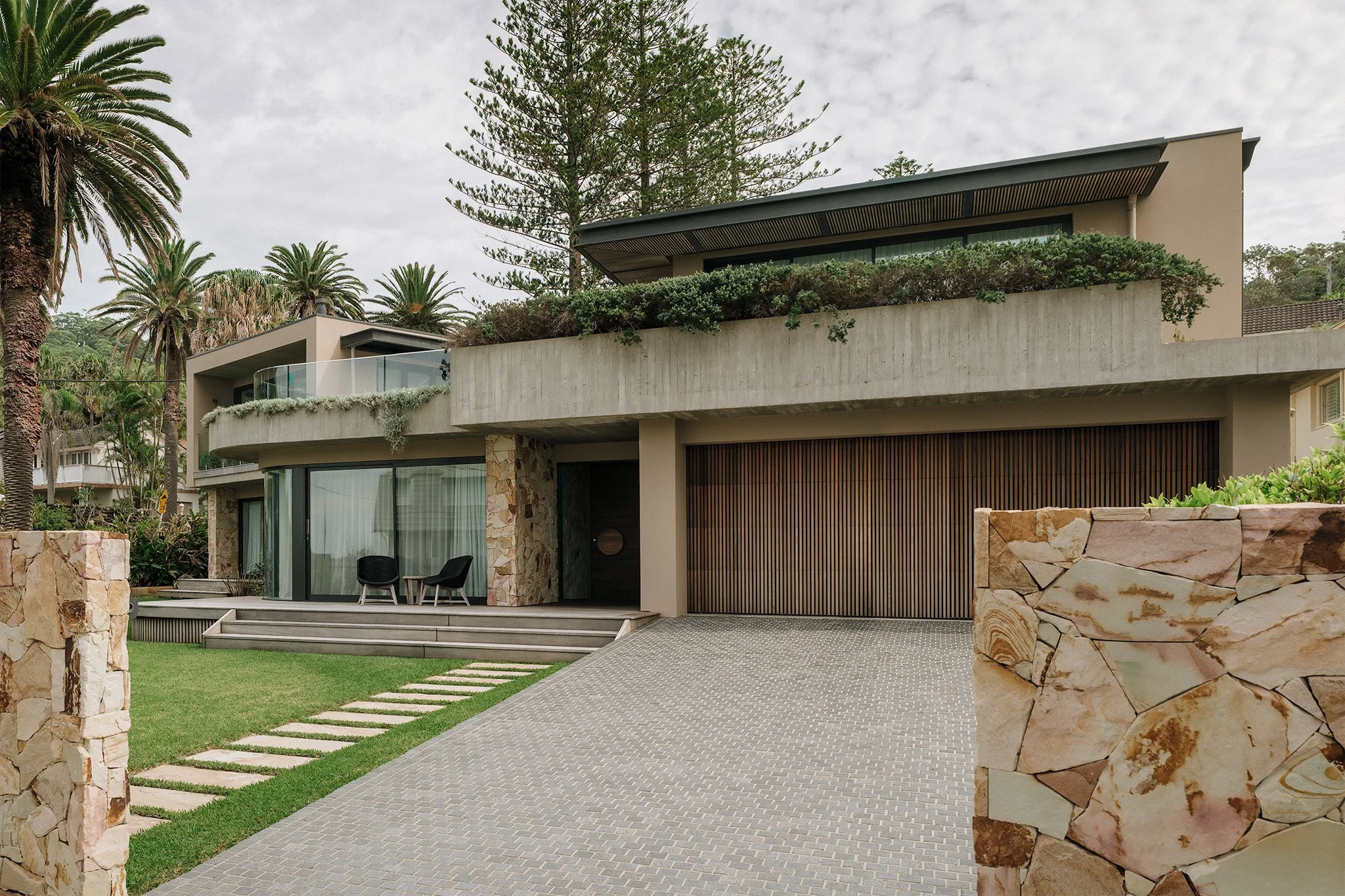 Architect-designed home on Sydney Northern Beaches with stone-clad exterior walls, large grassed landscape, and refined interior design.