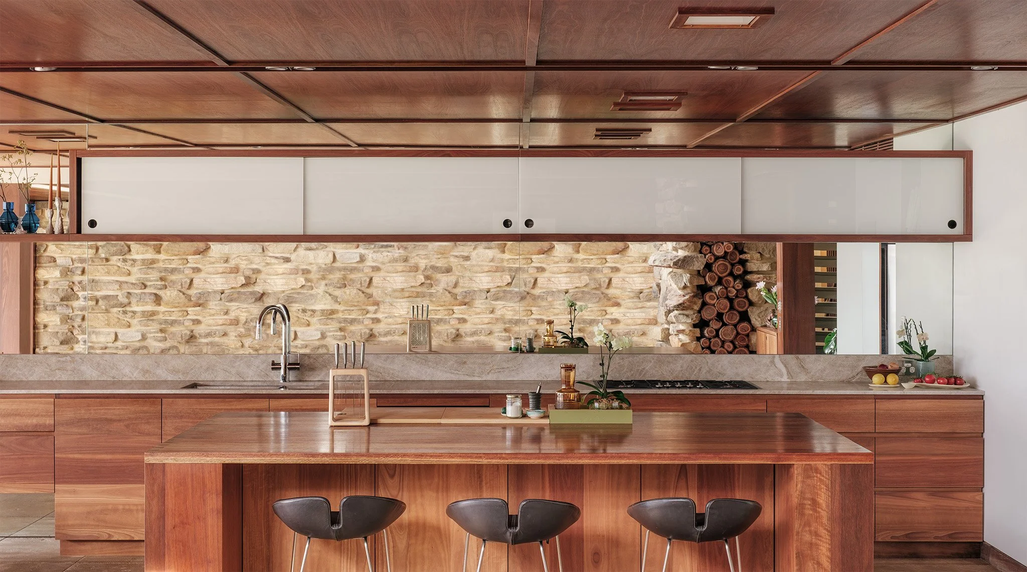 Contemporary kitchen with warm timber cabinets, a reflective mirror backsplash, and minimalist island seating.