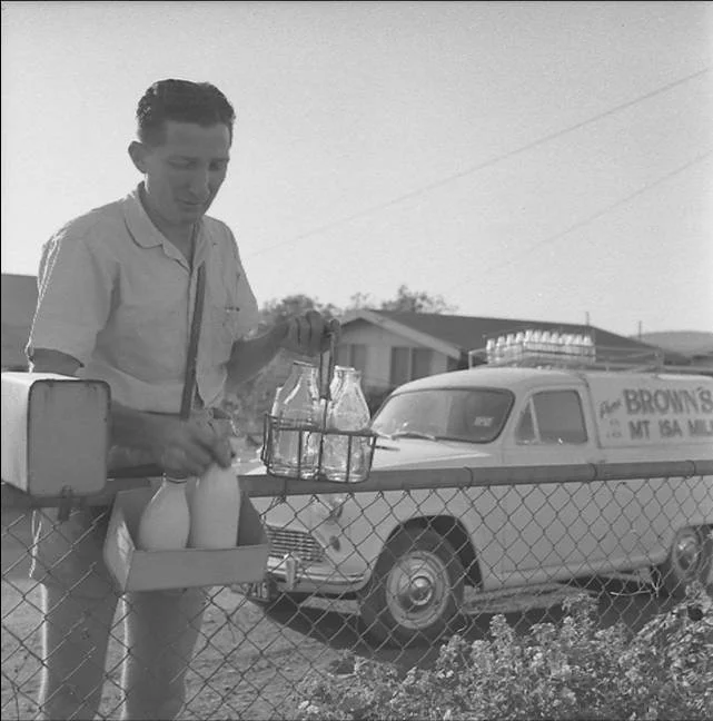 Historical Image of Mount Isa with a man at a roadside stand selling milk bottles, with a vintage truck in the background.