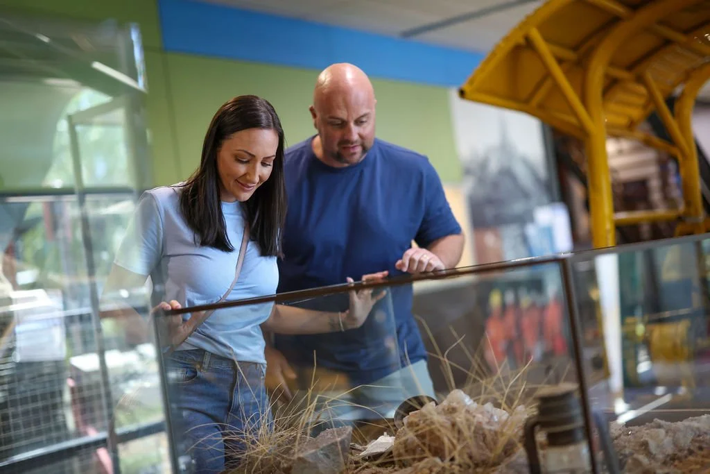 A woman and a man looking at a glass display case in the Isa Experience museum, with various objects inside.