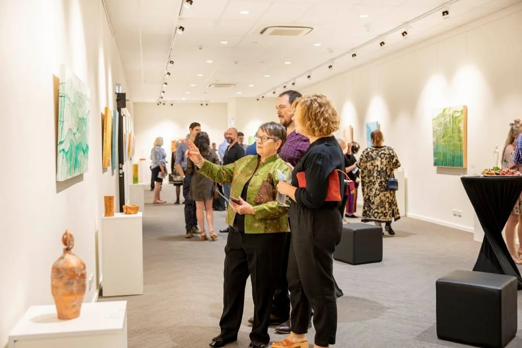 A group of people viewing modern artwork in an art gallery with white walls and track lighting.