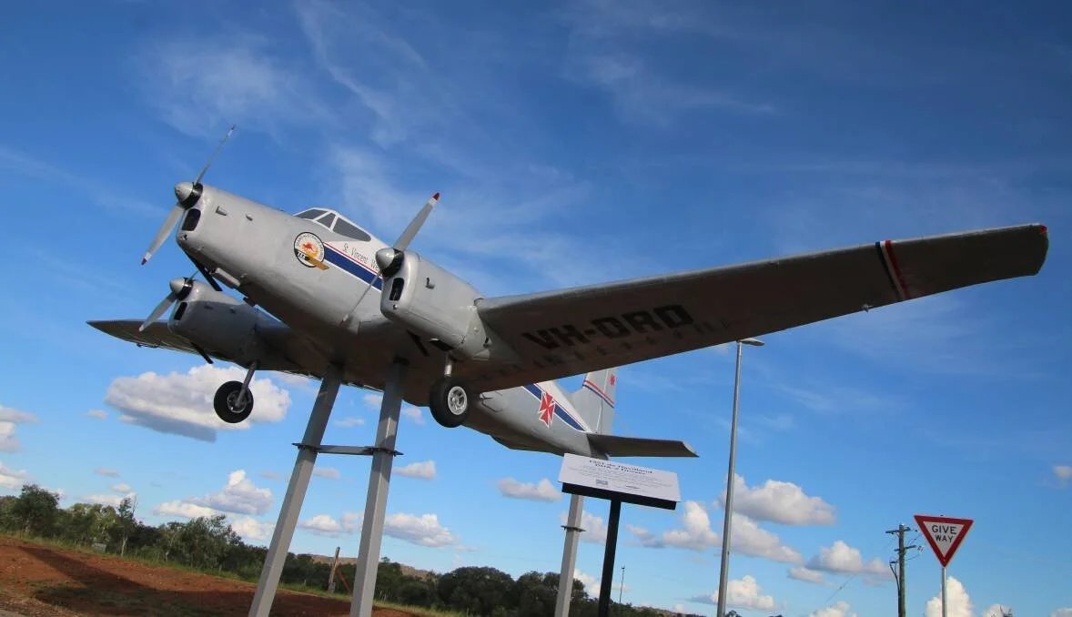 A RFDS Rover plane mounted on display stands outdoors under a blue sky with scattered clouds.