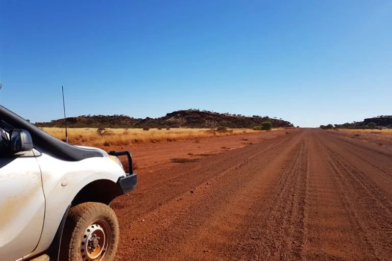 A white pickup truck parked on a dirt road in a desert landscape under a clear blue sky.
