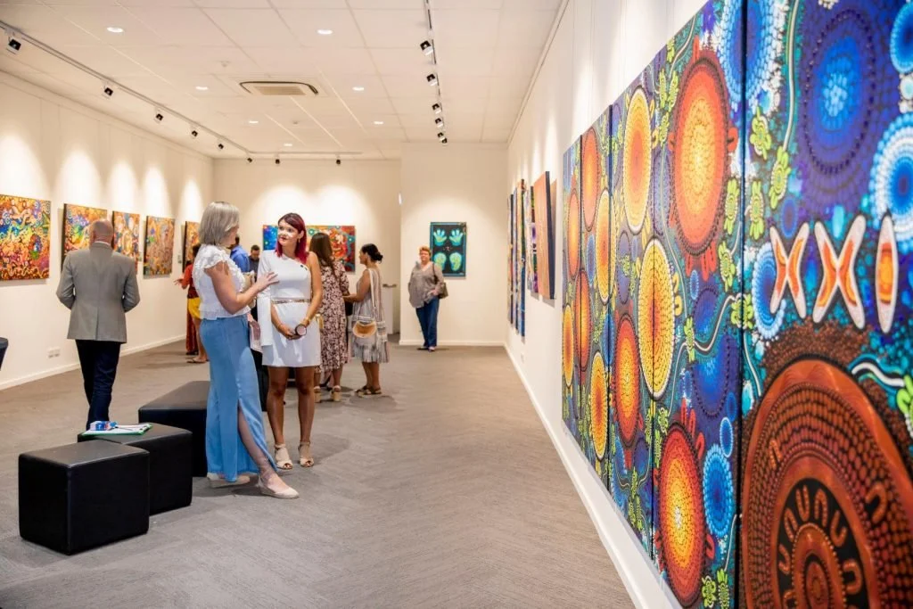 People viewing colorful abstract art paintings in an art gallery.
