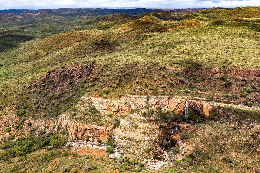 Aerial view of green rolling hills with a small waterfall cascading down a rocky cliffside.