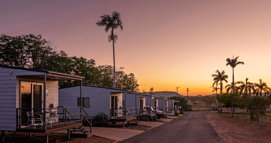 Row of small white houses with porches and chairs, palm trees, and a sunset sky.