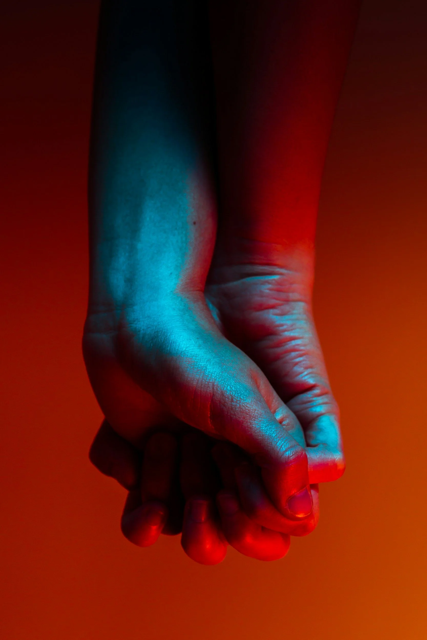 Hands with fingers intertwined in moody romance horror blue and red light