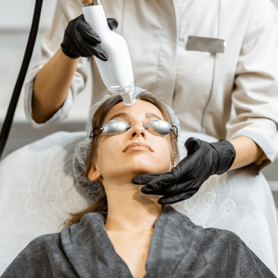 A woman receiving a facial treatment using a handheld device at a spa or clinic.