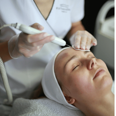 A woman receiving a facial treatment with a handheld device on her forehead, while lying down with her eyes closed.