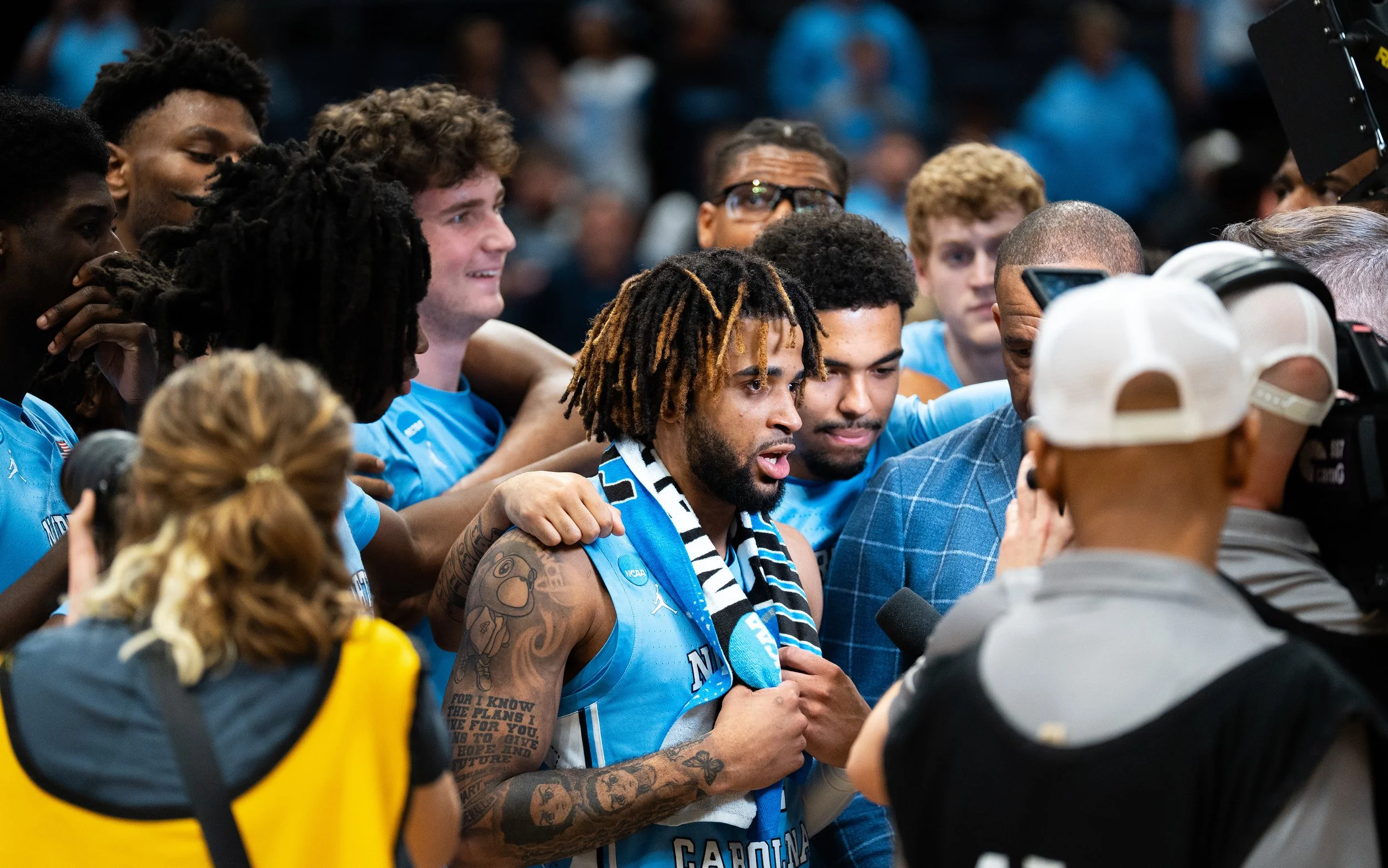 Group of MVP basketball players celebrating, wearing light blue jerseys, with some holding medals, surrounded by supporters and photographers.