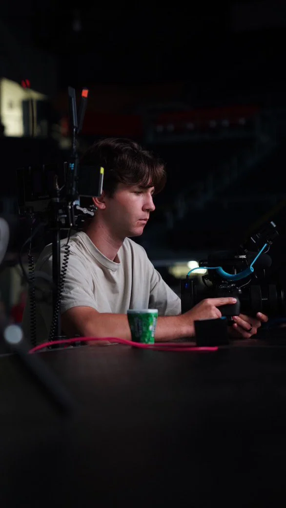 A young man operating a professional video camera in a dark environment.