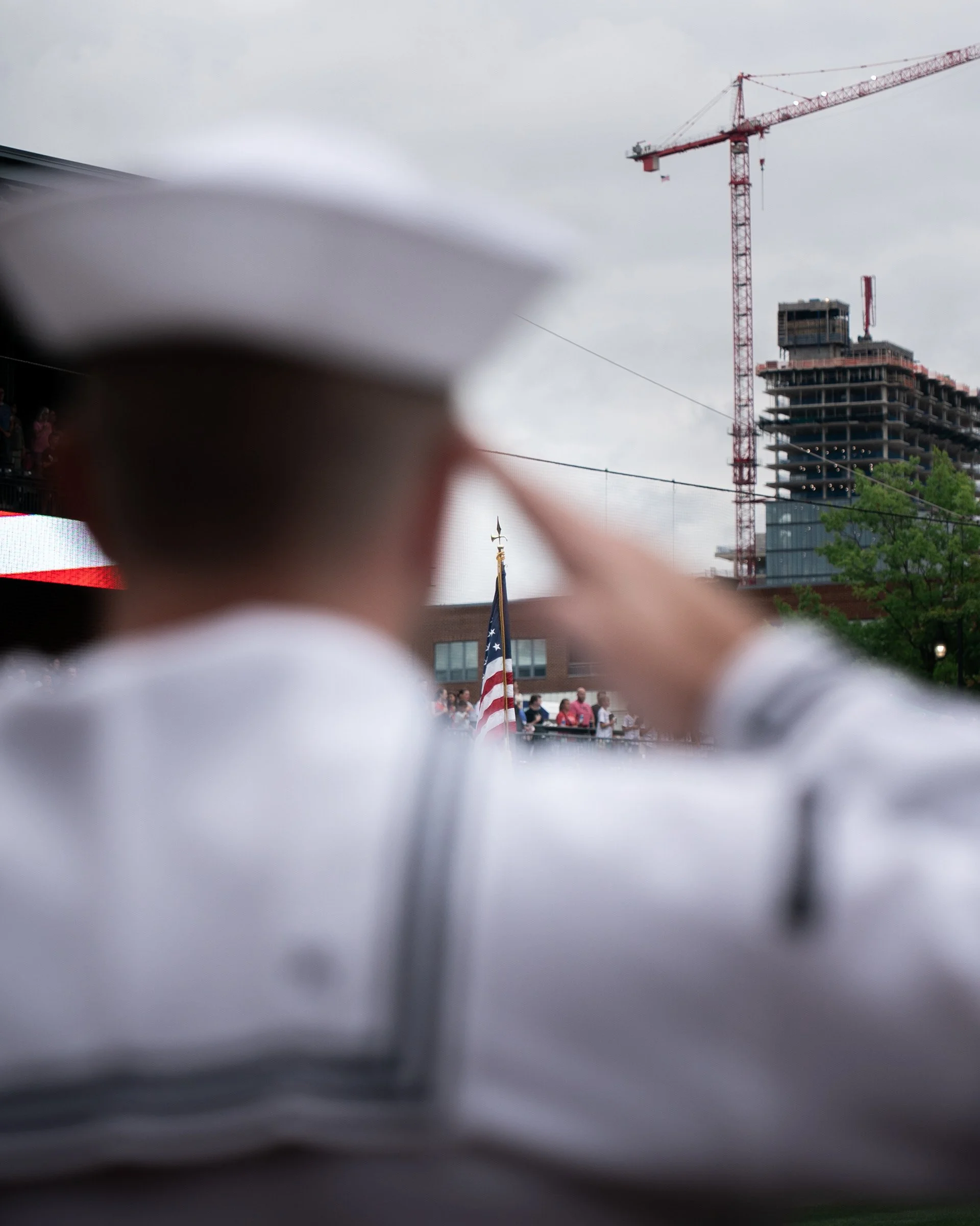 A construction site with a tall red crane and a skyscraper under construction, viewed through a blurred foreground.