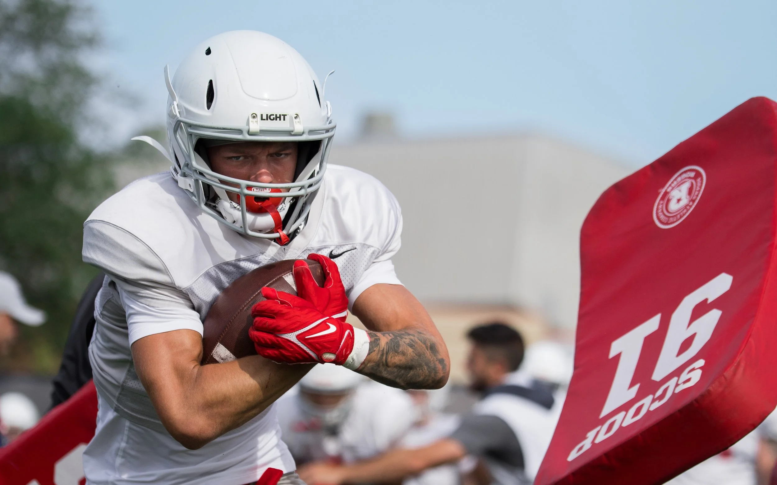 A football player wearing a white helmet and jersey, holding a football, and preparing to run during a game.