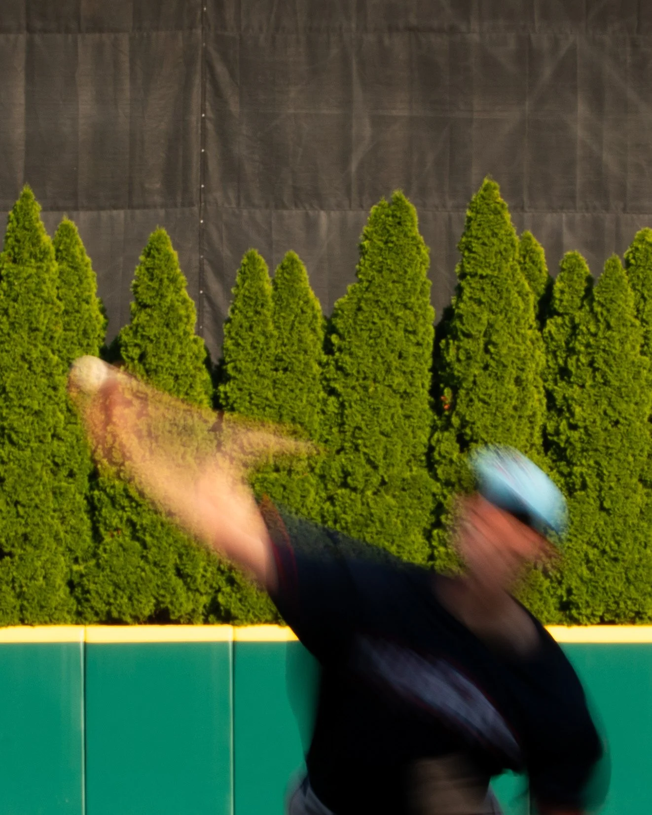 Blurred image of a person running past a large poster of green trees, with a black background.