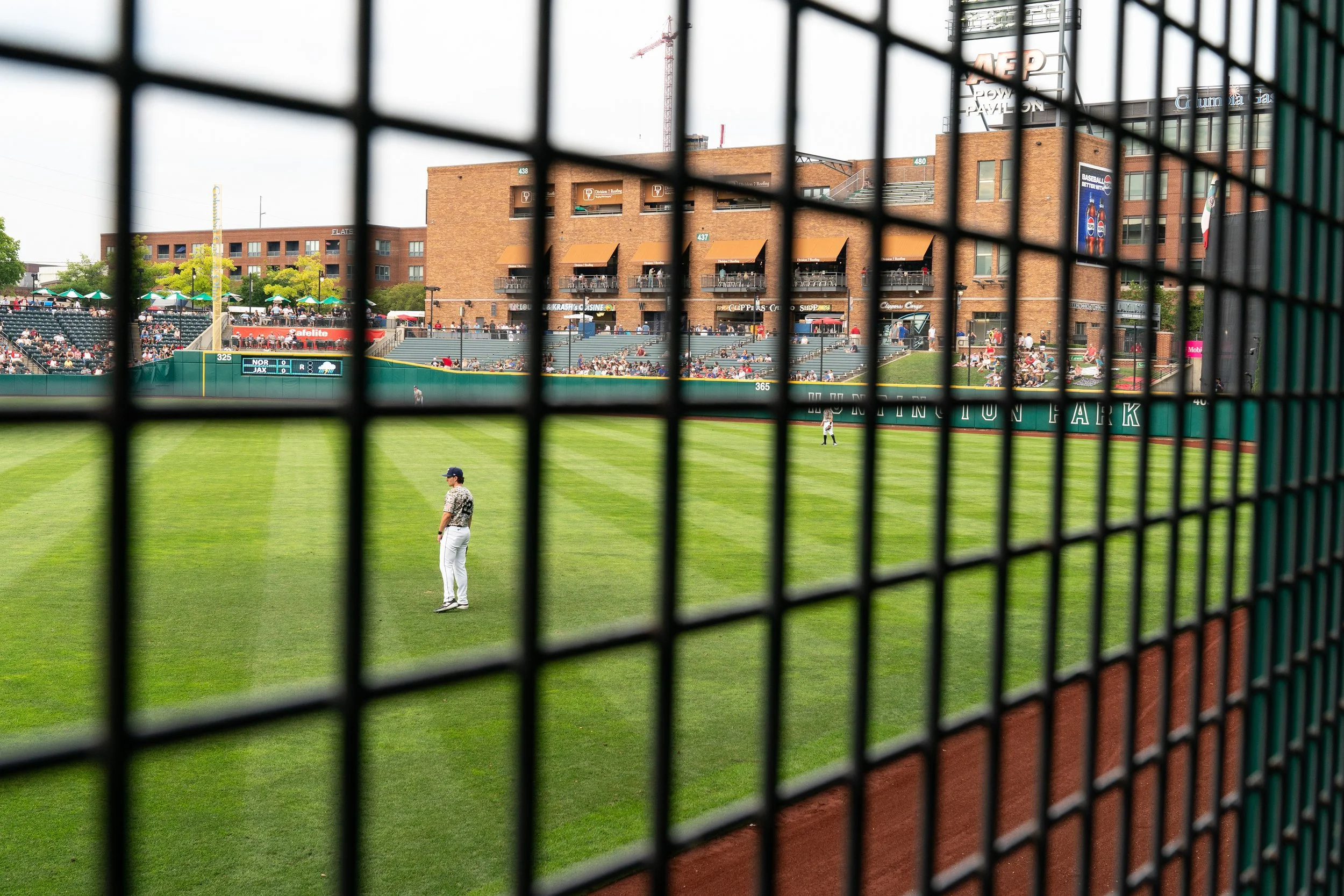 View of a baseball stadium through a black safety net, with players on the field and spectators in the stands during a game.