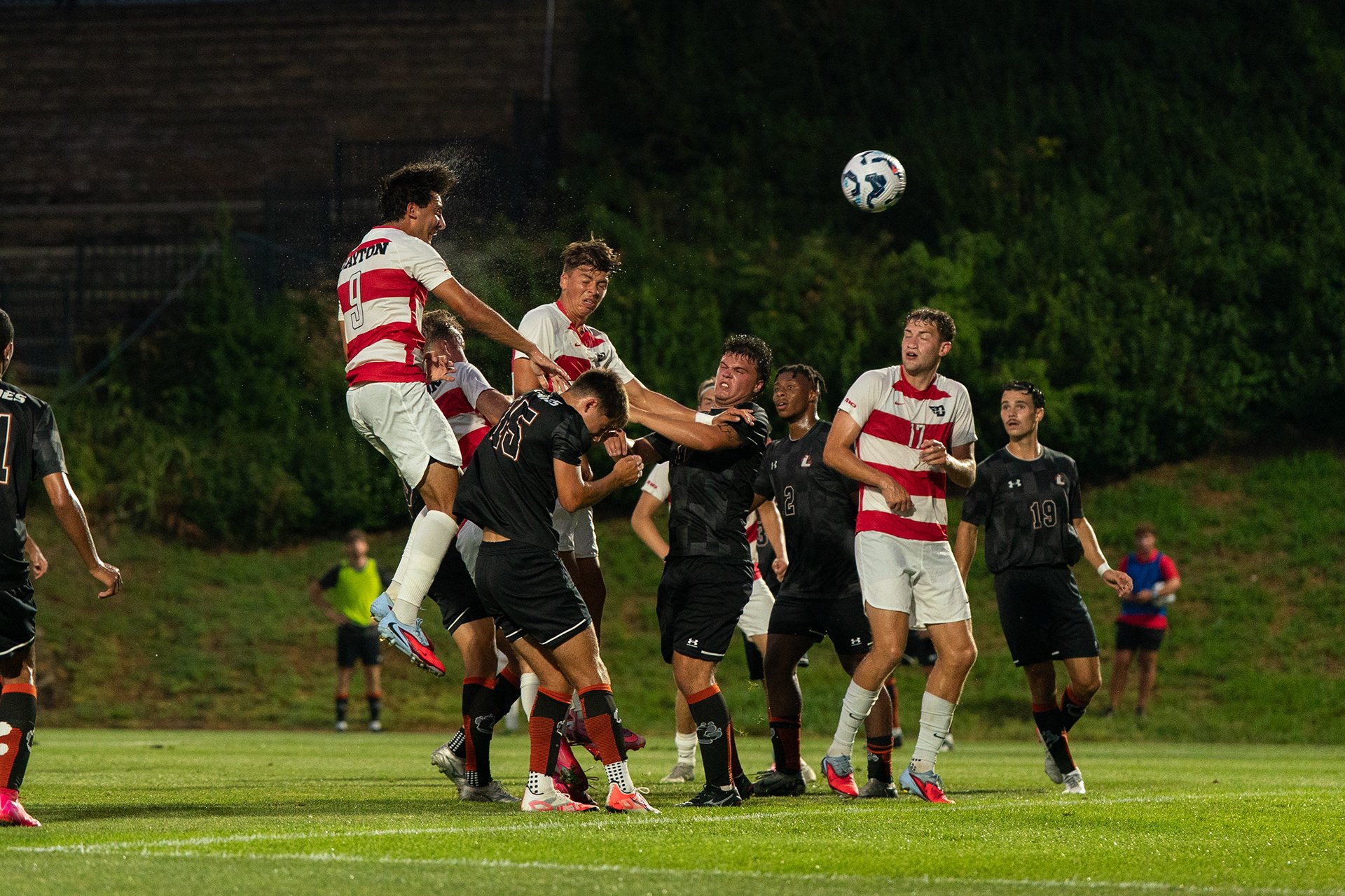 Soccer players in black and white jerseys compete for the ball under the night sky.