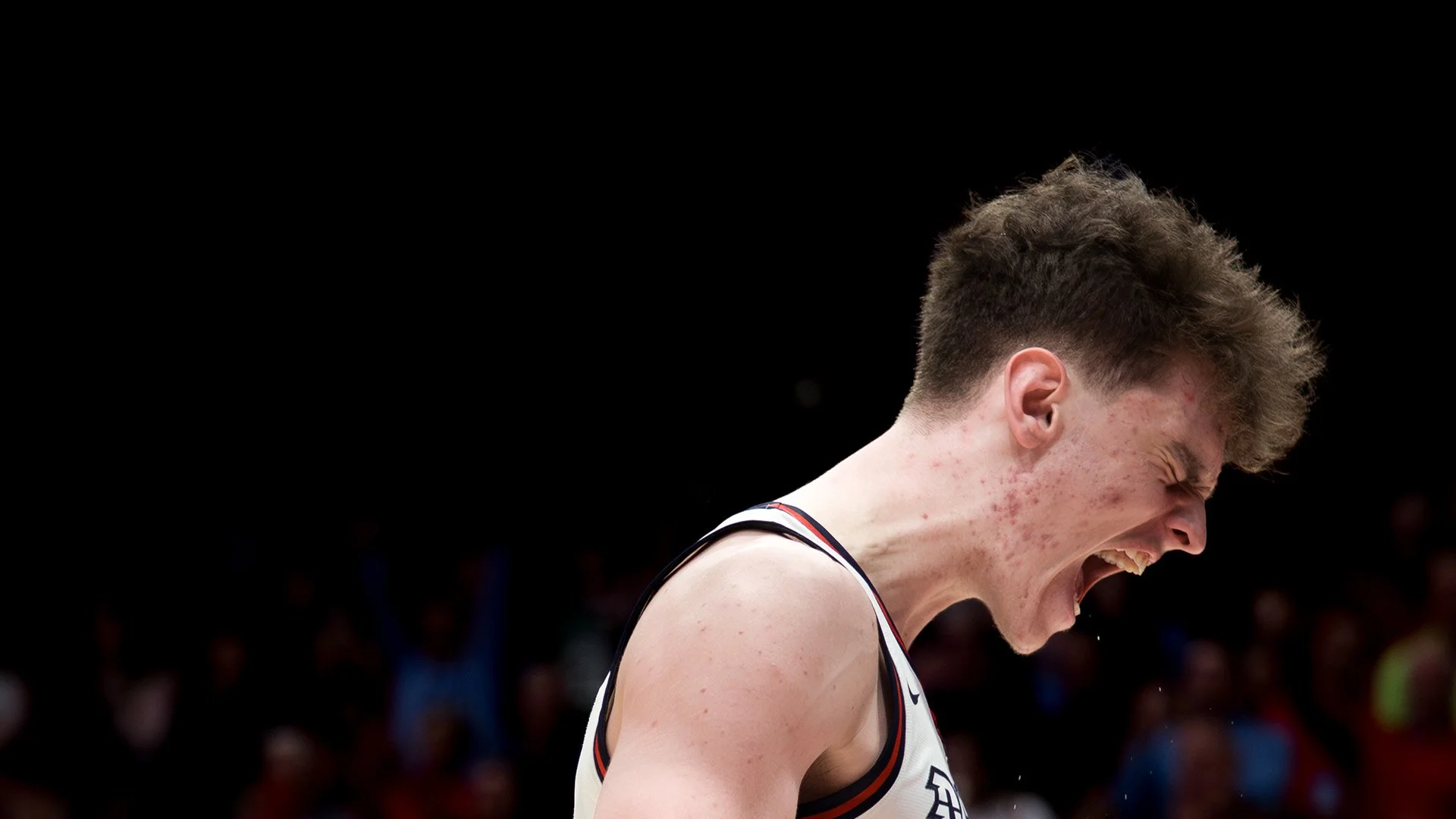 Young male basketball player with short curly hair, celebrating with mouth open, in a sleeveless jersey, on a basketball court.