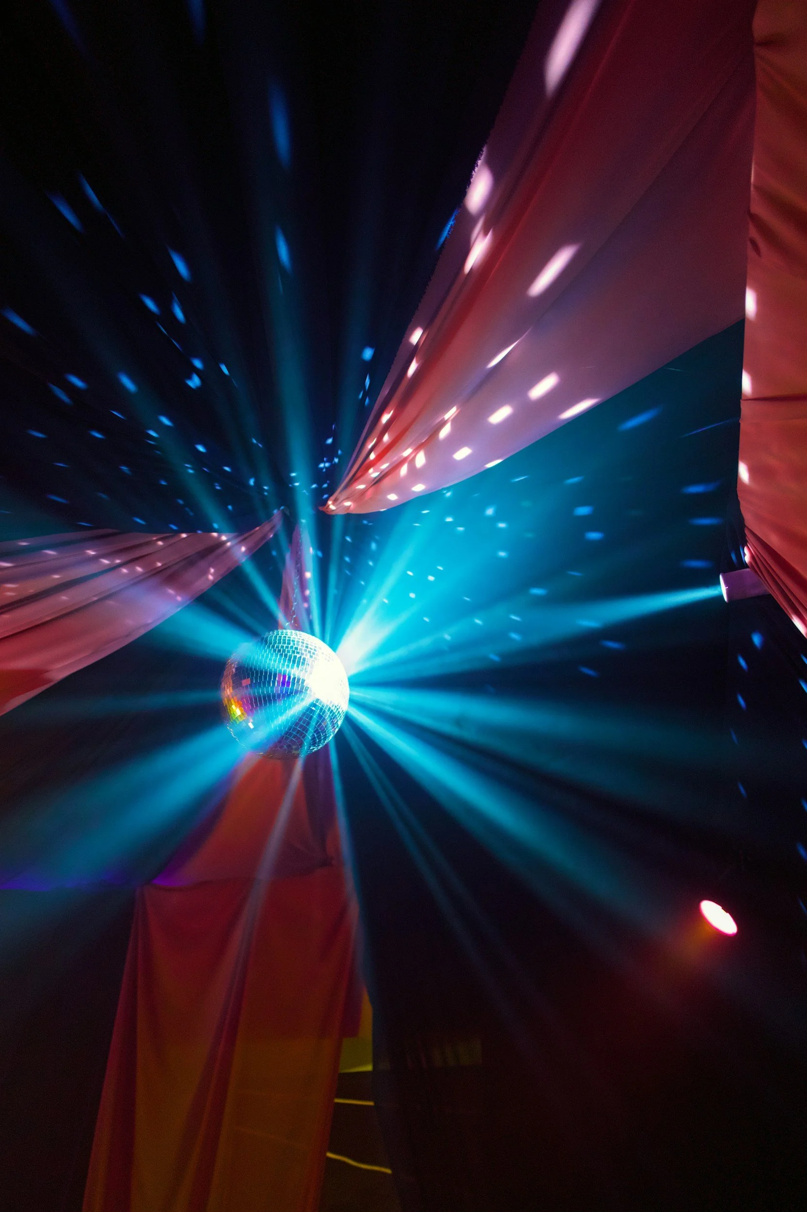 Disco ball with colorful lights and reflections, pink and blue lights illuminating the dark background with red and yellow curtains.