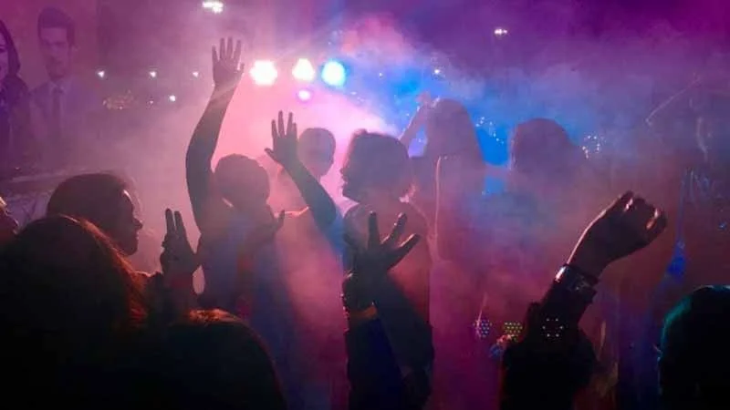 People dancing and enjoying music at a nightclub with colorful lights.