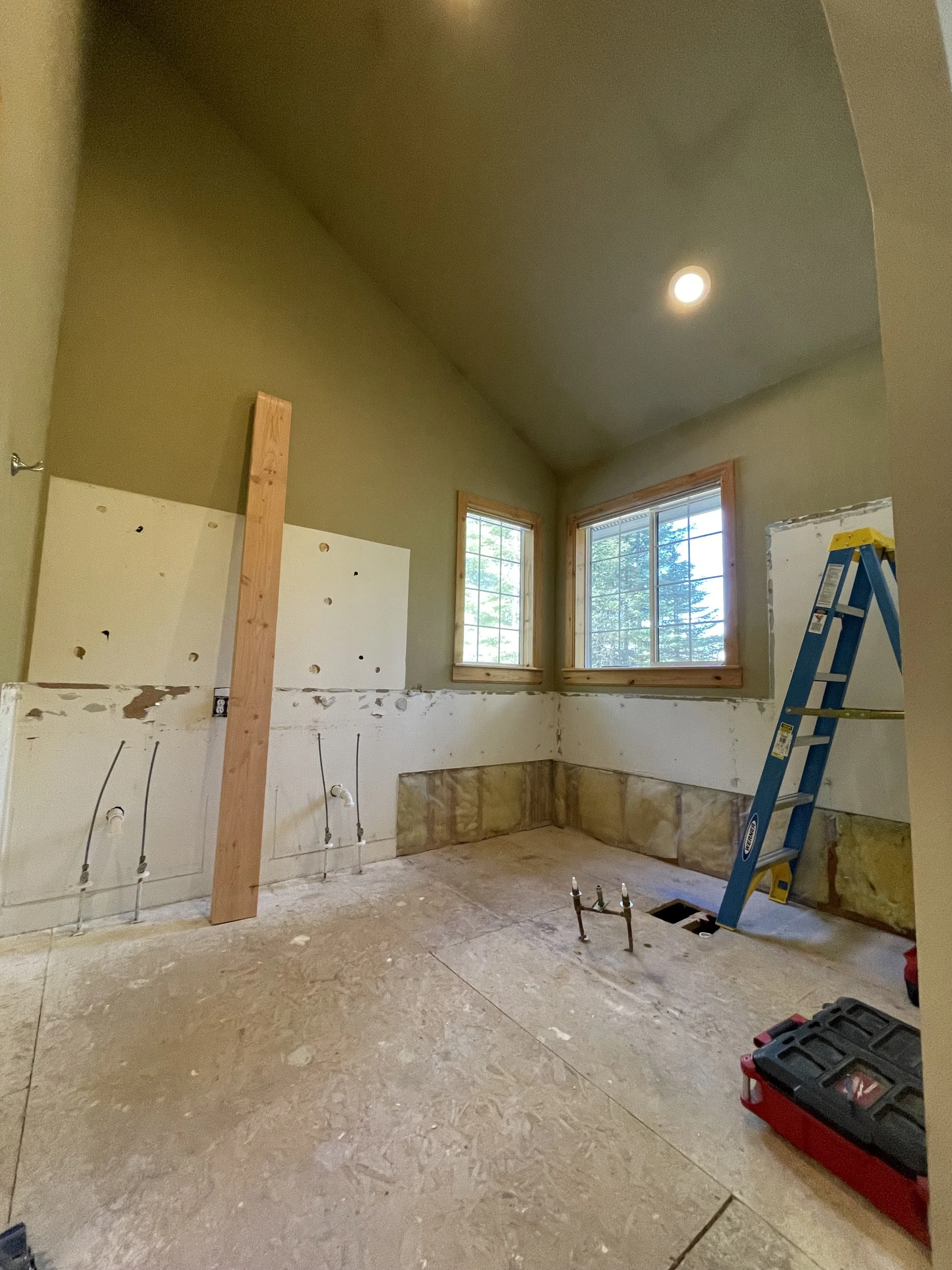 Room under renovation with exposed pipes and wiring, a step ladder, and construction tools, including a red toolbox.