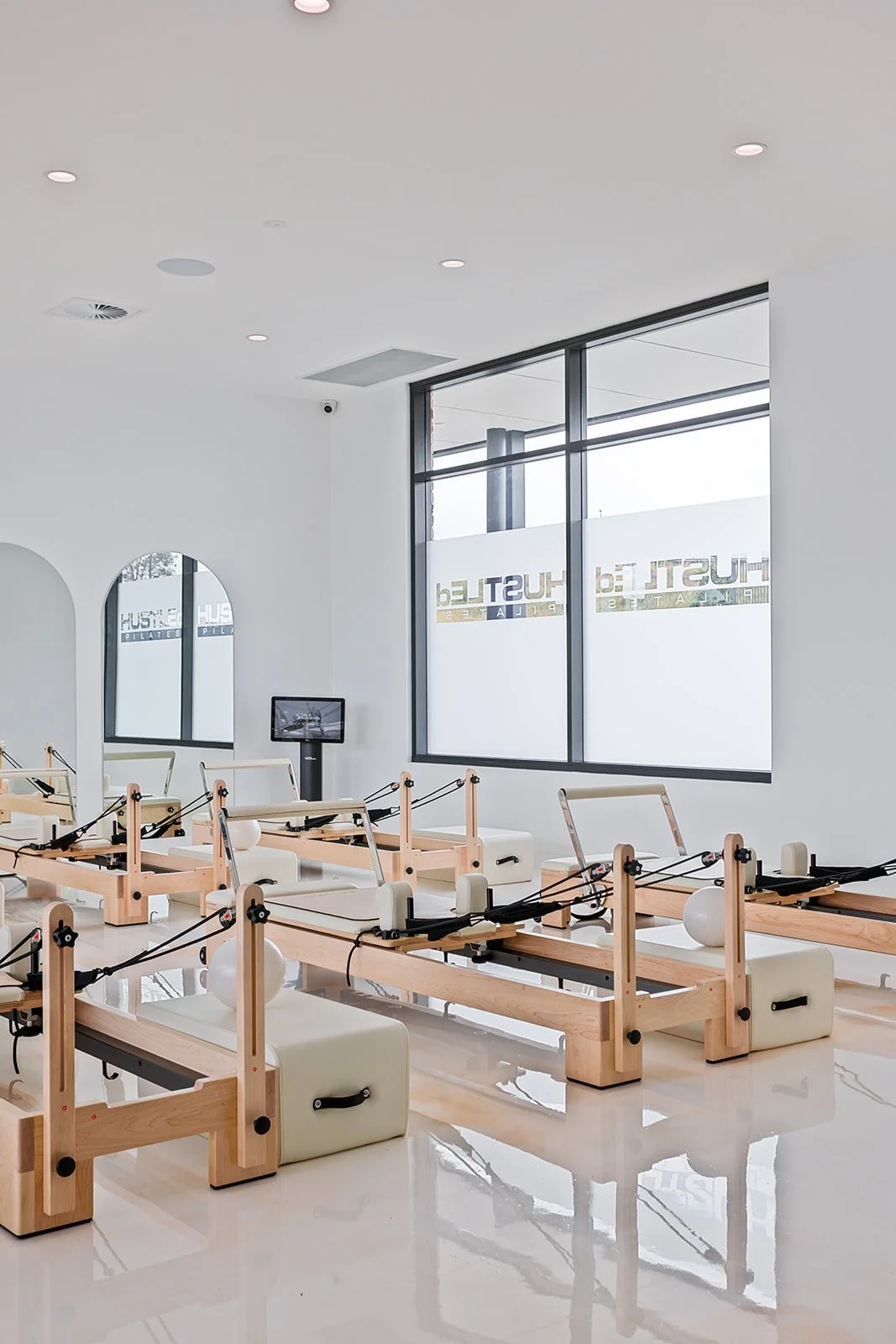 Pilates reformer machines in a bright, modern studio with large windows and minimal decor.