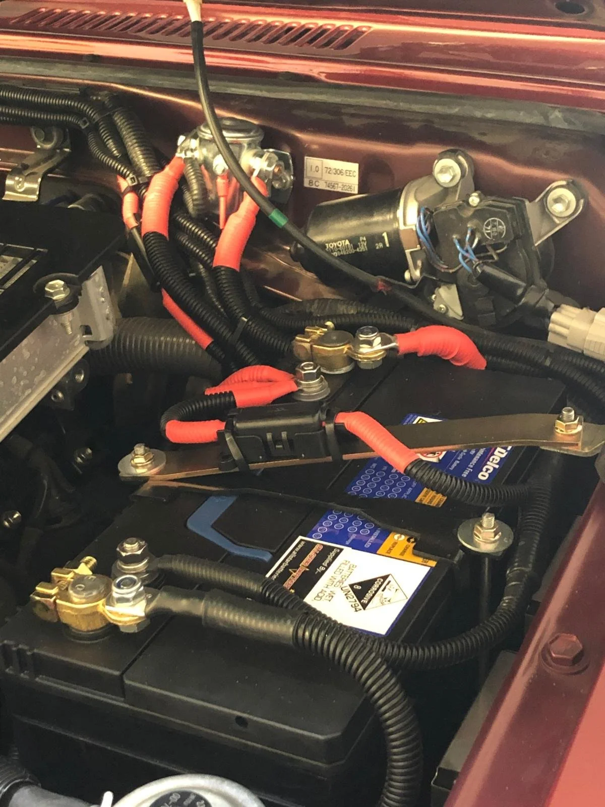 Close-up of a car engine bay showing wiring, a battery, and various mechanical components.