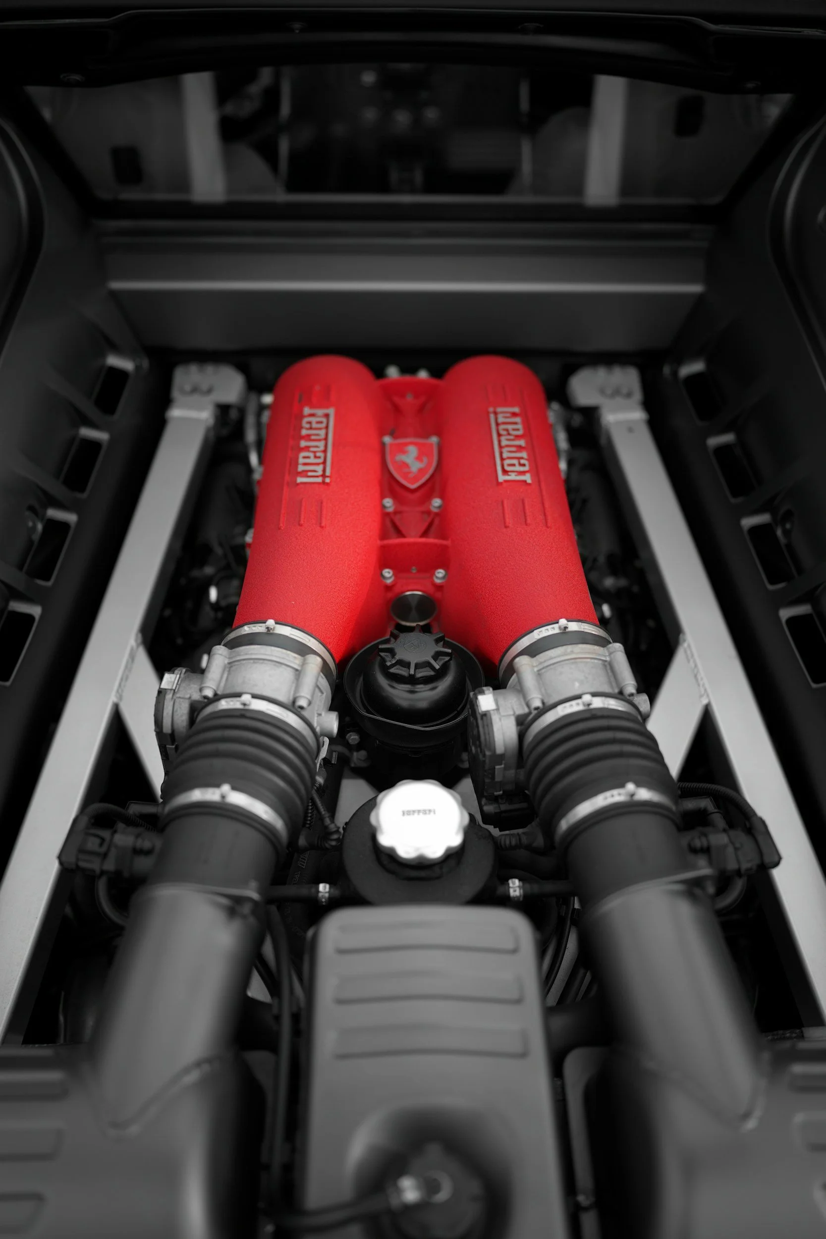 Close-up of a Ferrari engine with a red engine cover inscribed with the Ferrari logo and lettering, surrounded by black hoses and mechanical components.