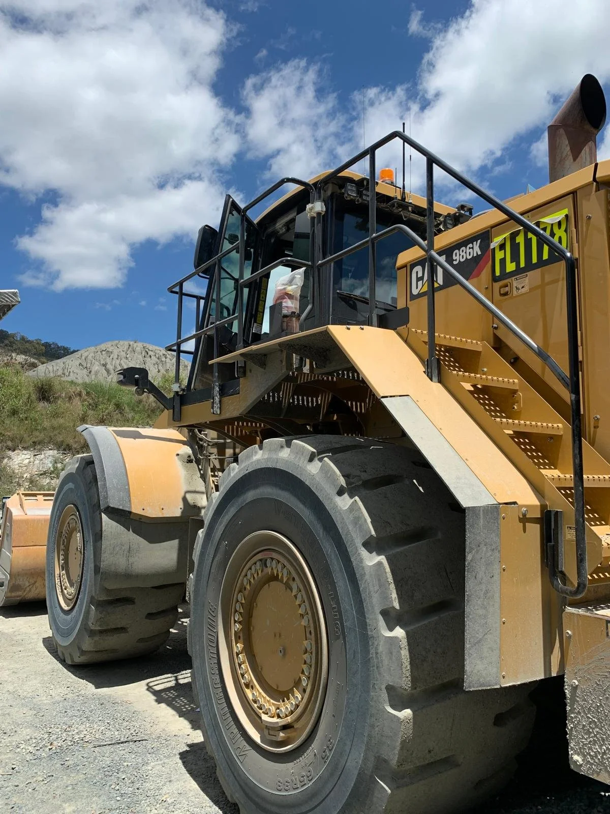 A large yellow Caterpillar 986K wheel loader with oversized tires on a construction site, under a partly cloudy sky.
