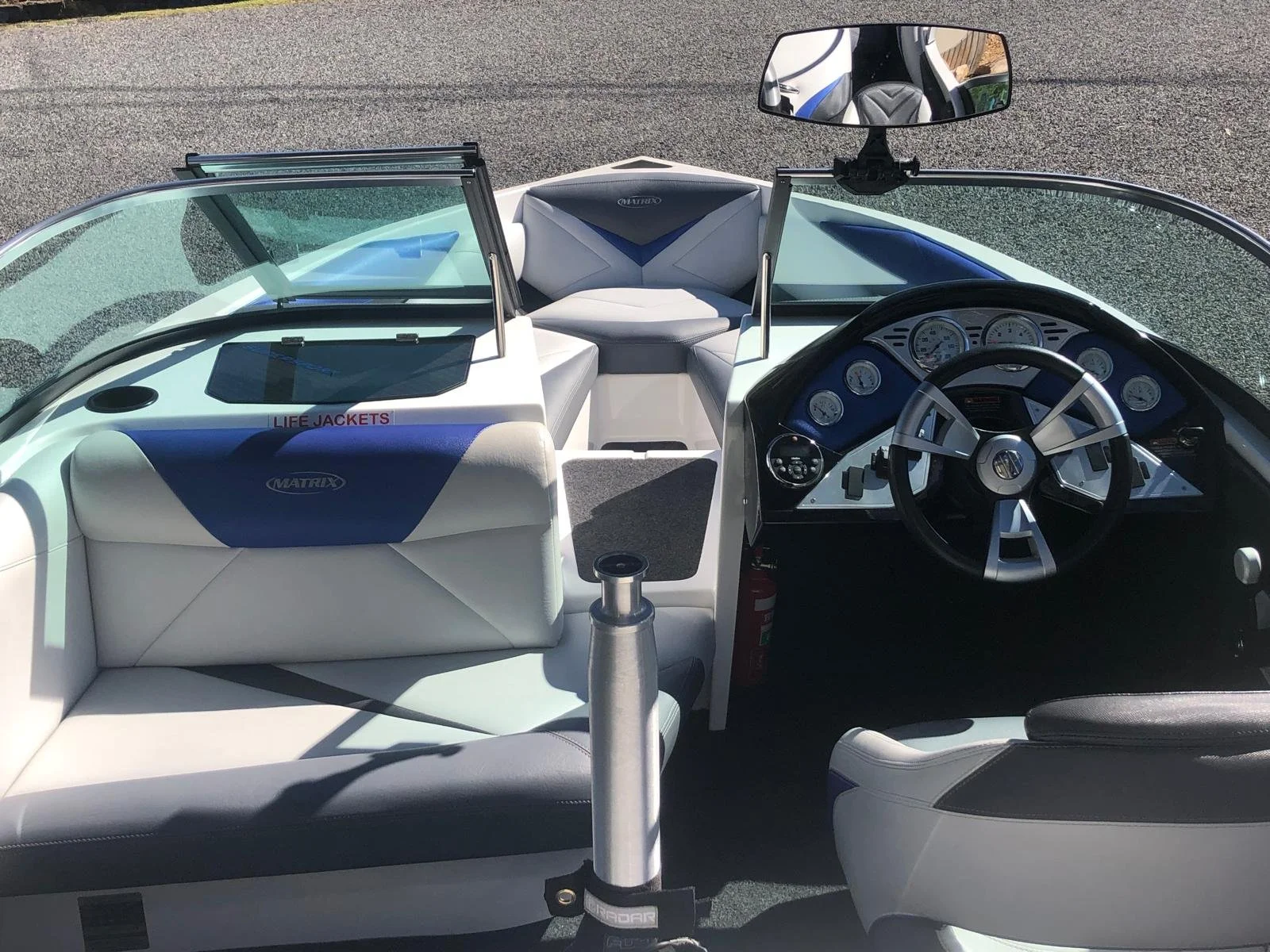Interior view of a white and blue motorboat, showing the steering wheel, dashboard, and seating area with a rearview mirror and a fire extinguisher.