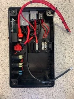 Open electronic enclosure with red and black wires, connectors, and circuit components inside.