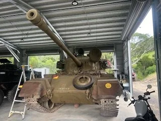 Military tank inside a garage with a motorcycle parked nearby.